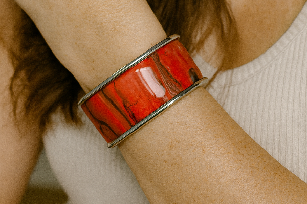 Close-up of a person wearing red and silver bangle bracelet on their wrist.