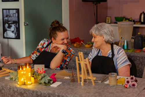 Mother and daughter sitting at a table painting. Smiling and relaxing